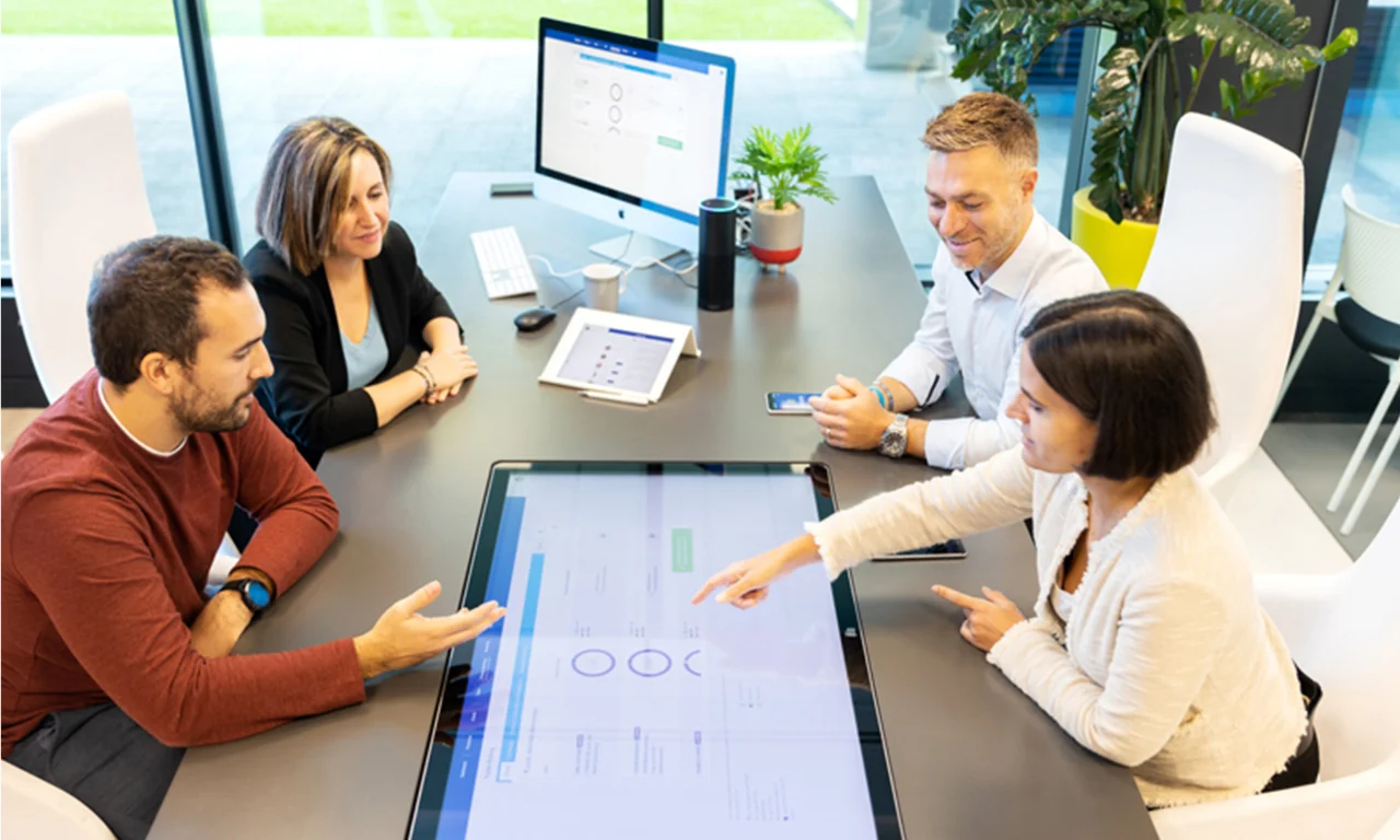 Eine Gruppe von Fachleuten arbeitet kollaborativ in einem modernen Innovationslabor, das digitale Tools und interaktive Displays nutzt, um greifbare Ergebnisse zu erzielen.